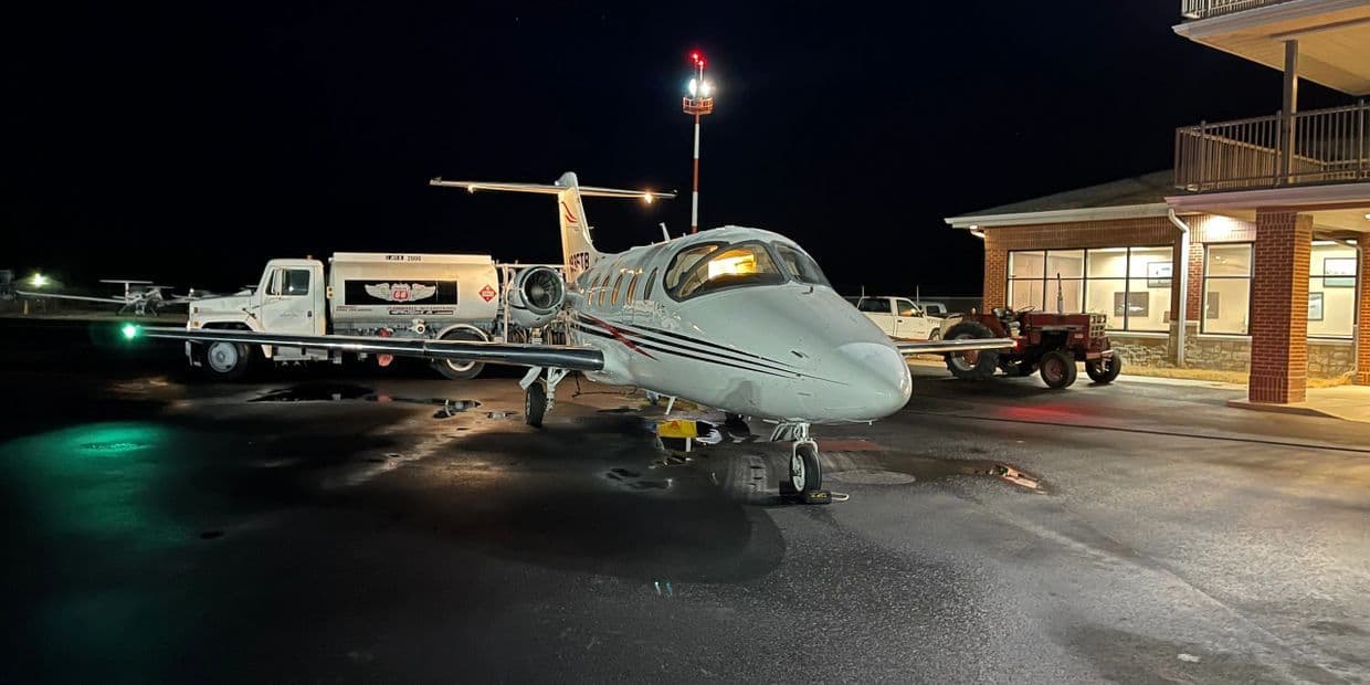 A business jet and a fuel truck on the wet ramp outside the Don Davis Aviation FBO building at night