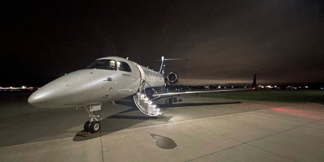 A silver business jet on the ramp at night with its airstair lowered