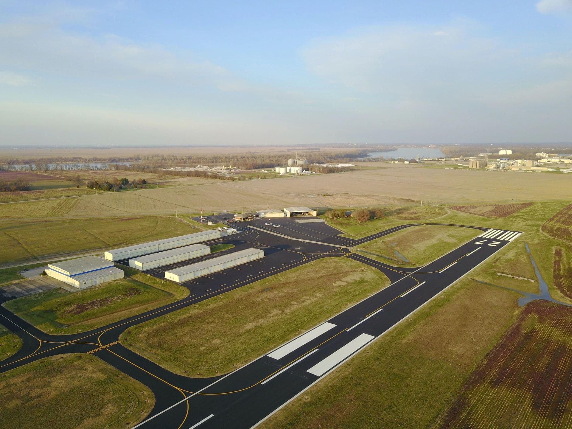 Aerial view of Henderson City-County Airport: the runway, taxiways and rows of hangars among farm fields, with the Ohio River on the horizon